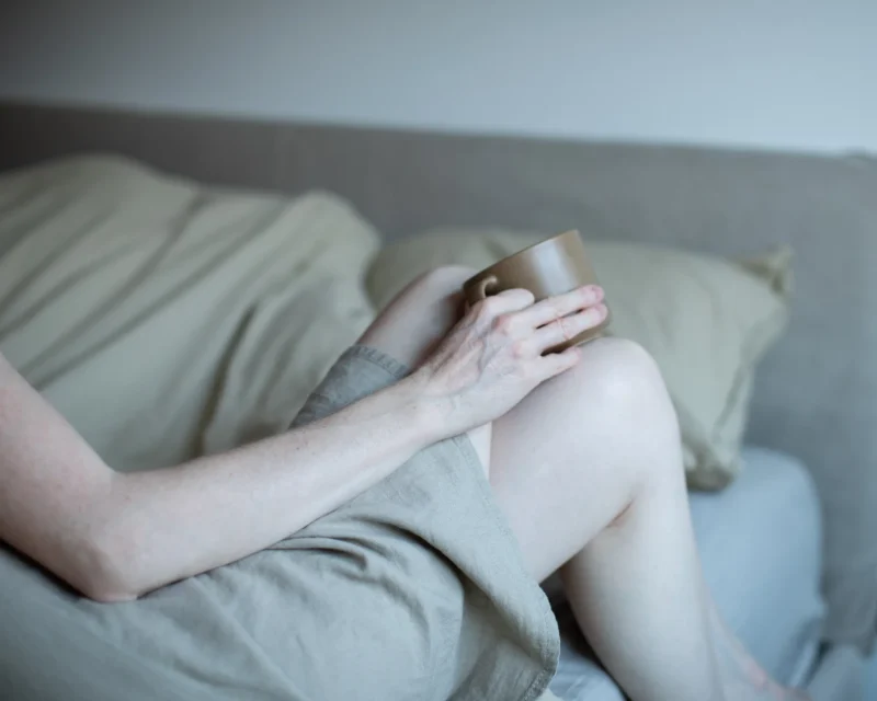 Woman sitting with knees drawn up, holding a ceramic mug