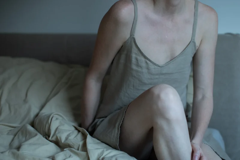 Woman sitting on the edge of a bed in a linen slip dress